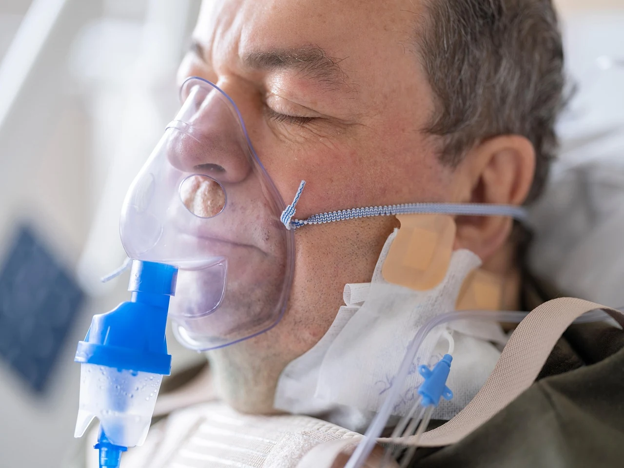 Man in a hospital bed wearing a nebulizer oxygen mask while receiving emergency care for anaphylaxis