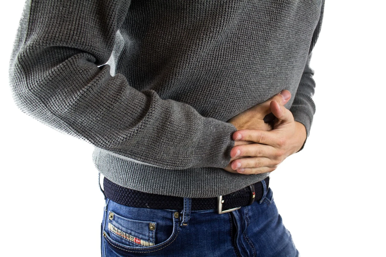 Man in a gray sweater clutches his lower abdomen with both hands, a typical pose in appendicitis pain