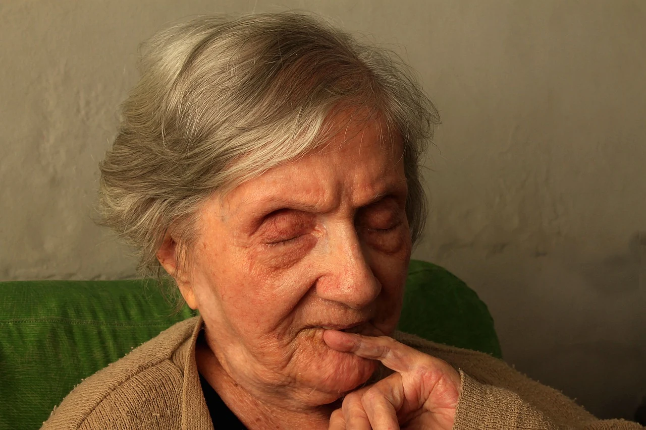 Elderly woman with eyes closed and a finger to her lips, lost in thought, illustrating memory loss and aging