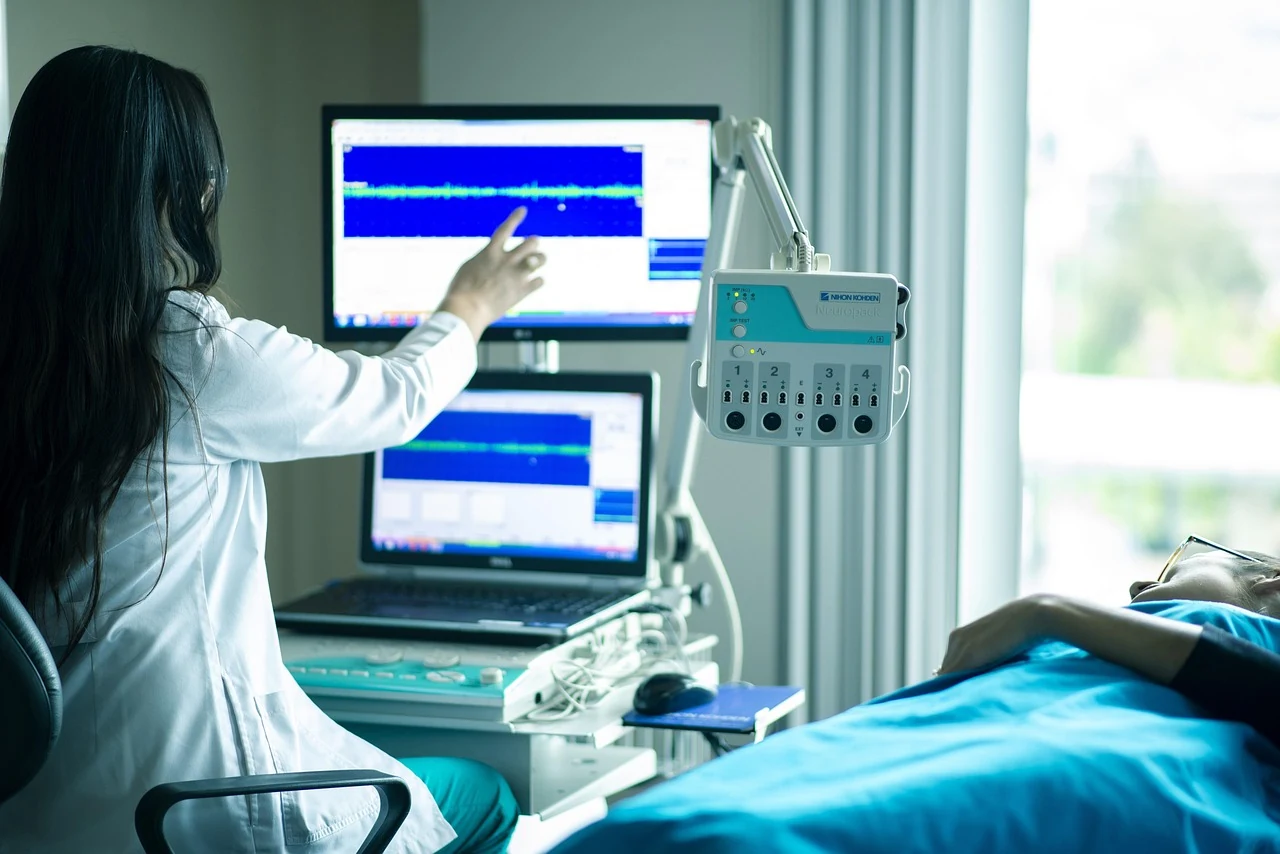 Doctor points at a monitor screen in a diagnostic room while a patient lies on a couch before a gastroscopy