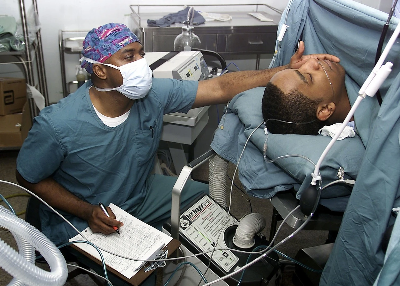 Anesthesiologist in a mask and surgical cap monitors a patient under anesthesia before planned surgery