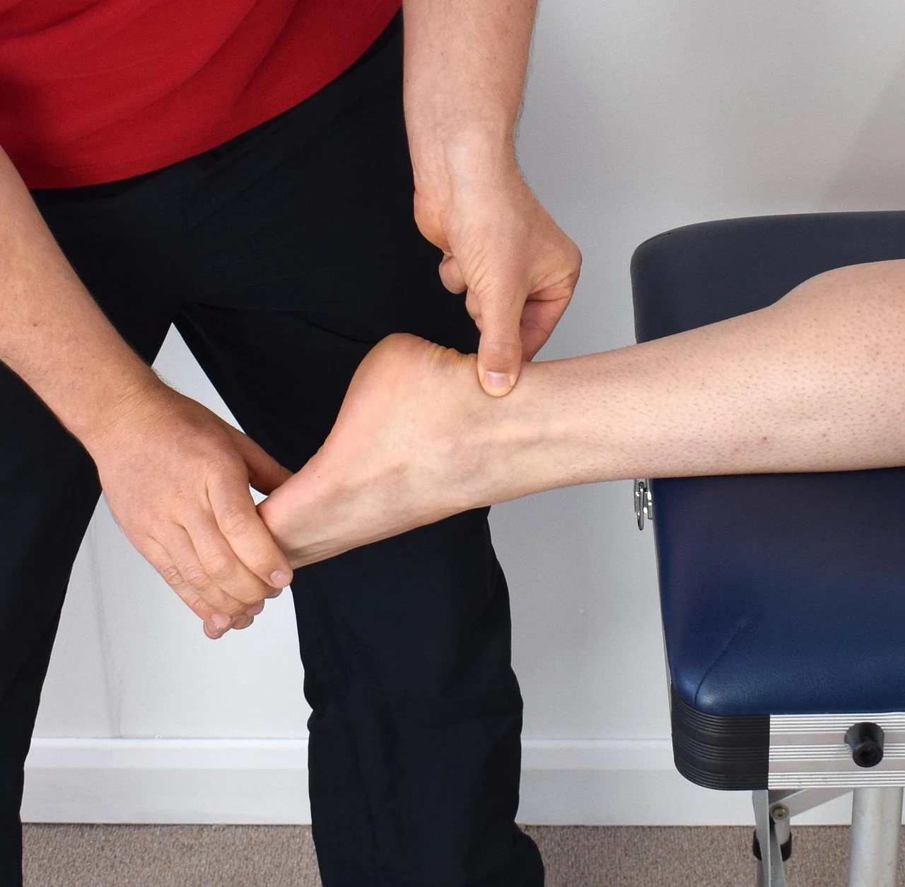 Clinician examining a patient's ankle with both hands on an exam table to tell a sprain from a fracture
