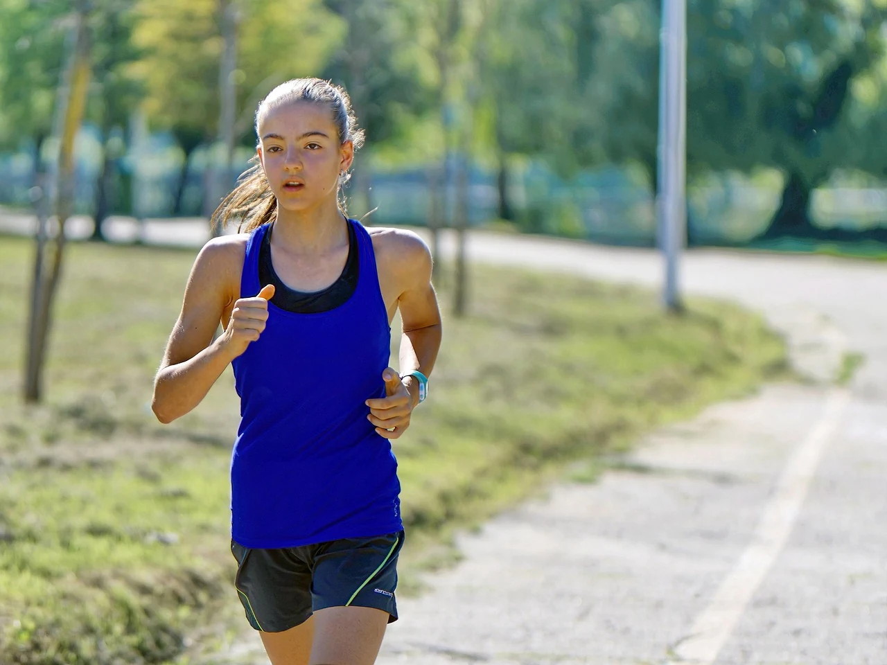 Girl in a blue tank top jogs along a park path, a moderate workout that is good for the heart