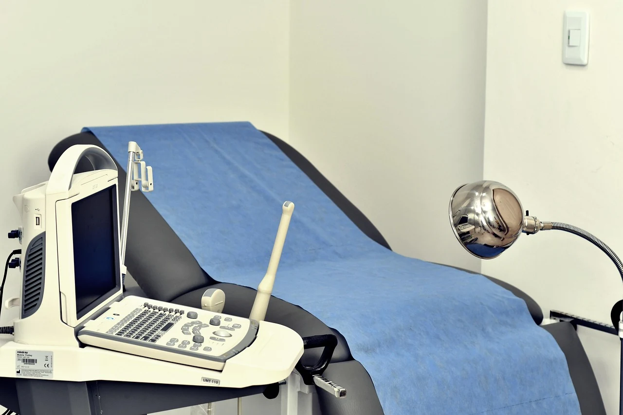Gynecology exam room with a couch under a blue sheet, an ultrasound unit, and a lamp for cervical screening