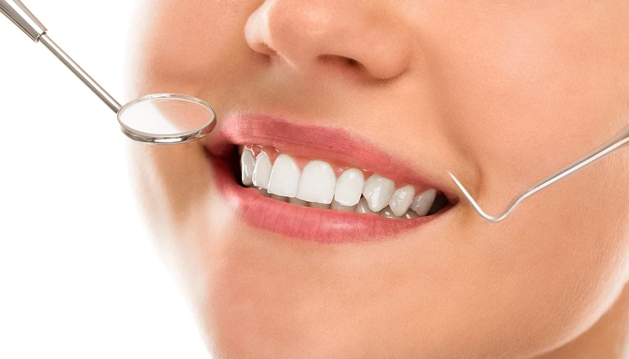 Smile with even white teeth and a dental mirror and probe near the lips after teeth whitening