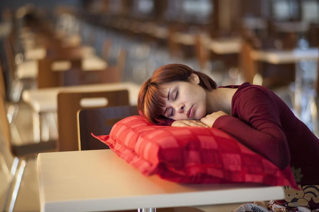 Exhausted woman sleeps with her head on a pillow on a cafe table, a sign of constant fatigue that may be hormonal