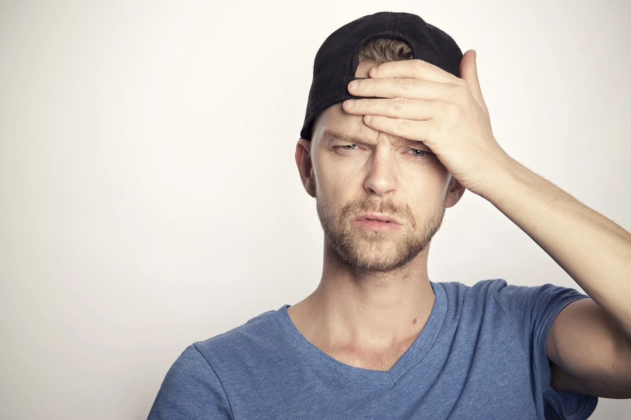 Man in a backward cap frowning with his hand on his forehead as if feeling dizzy