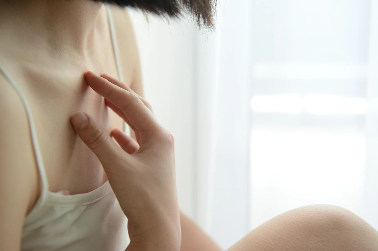 Woman in a white camisole touches her fingers to the area near her collarbone, checking for enlarged lymph nodes