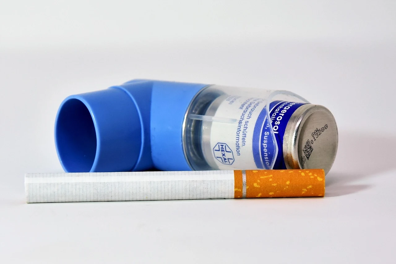 Blue asthma inhaler lying next to a cigarette, a reminder of how smoking harms the lungs in pulmonology
